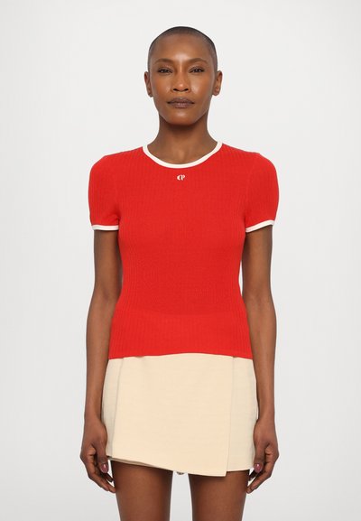 Haut en tricot côtelé rouge avec bord blanc, associé à une jupe portefeuille beige. Le haut présente une coupe ajustée et des manches courtes.