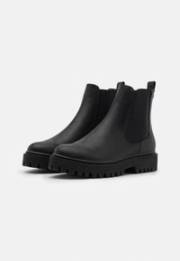 Black leather ankle boots with elastic side panels and a textured, thick sole featuring deep grooves for traction.