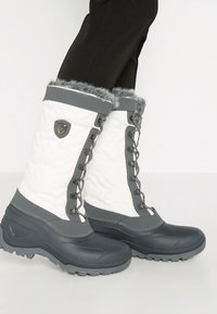 Botas impermeables gris y blancas con tela acolchada, ribete de piel sintética en la parte superior y diseño de cordones. Suela de goma duradera para tracción.