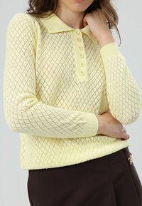 Lichtgele gebreide trui met een ruitpatroon, geribde kraag en een knopenlijst. Lange mouwen met geribde boorden.