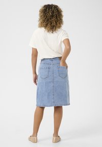 Denim midi-rok in lichtblauw, met een aansluitende taille, twee achterzakken en subtiele stiksels. Ggedragen met een beige top en schoenen.
