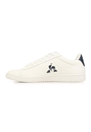 Basket basse blanche avec lacets blancs, languette de talon noire et logo coq noir sur le côté sur fond blanc.