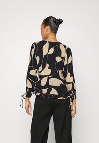 Top a manica lunga con motivo nero e beige, con cordini regolabili ai polsini e orlo arricciato. Tessuto morbido con design astratto.
