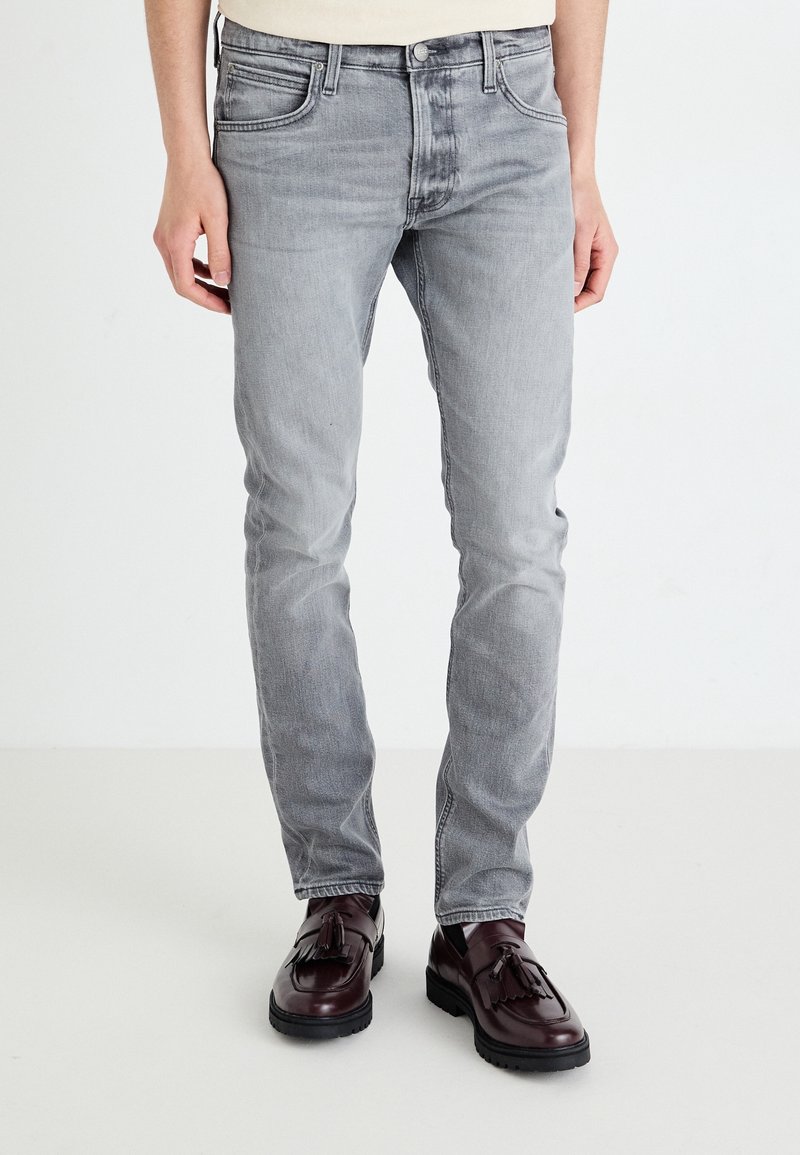 Jeans de denim gris claro con corte slim, cinco bolsillos y un leve desgastado, combinados con mocasines de borlas burdeos oscuros.