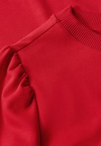 Felpa rossa con collo a costine e maniche a sbuffo. Tessuto liscio di colore uniforme con dettagli di cucitura sottili.