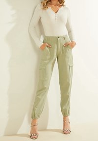 Vaaleanvihreät cargo-housut, joissa on joustavat hihansuut ja läpälliset taskut, yhdistettynä ribbattuun valkoiseen pitkähihaiseen paitaan ja kuvioituihin korkokenkiin.