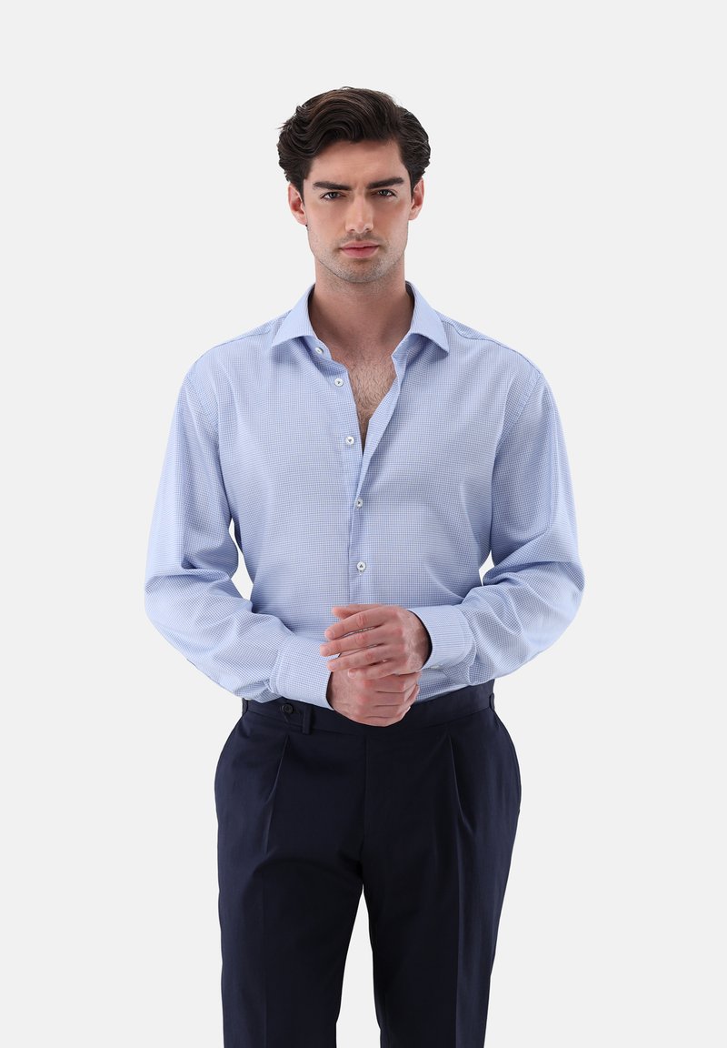 Camicia a scacchi blu chiaro con vestibilità su misura, colletto button-down, maniche lunghe e bottoni bianchi, abbinata a pantaloni scuri.