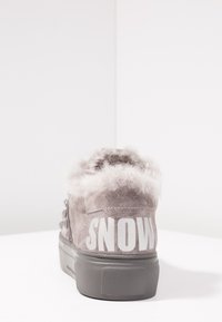 Baskets en daim gris avec doublure duveteuse et inscription « SNOW » en blanc sur le talon, présentées sur une surface blanche avec un fond blanc.