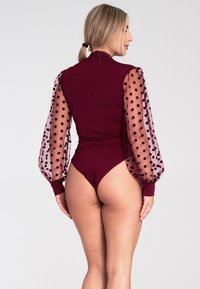 Burgundowy body z przezroczystymi rękawami w grochy, dopasowany krój i wysoki stan nogawki. Gładki materiał z teksturowanymi akcentami.