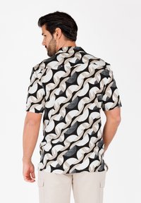 Camisa de manga corta con un patrón abstracto de olas en negro, blanco y beige. Presenta un cuello y un corte holgado, fabricada con un tejido ligero.