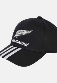 Gorra de béisbol negra con un logo de helecho blanco y el texto "ALL BLACKS". El diseño incluye tres franjas blancas en la visera. Material de algodón.