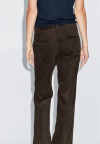 Bruine corduroy broek met een rechtvallende pasvorm, voorzien van achterzakken, gestructureerde ribbels en een tailleband. Geen zichtbare hardware.