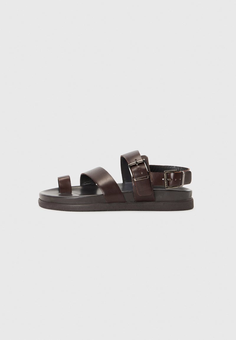 Brown leather sandals with open toe, two wide straps, and adjustable buckle. Flat sole with subtle texture and cushioned footbed.