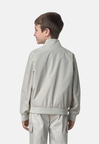 Giacca bomber grigia chiara con colletto rialzato, polsini ed orlo elasticizzati. Texture morbida e liscia con una finitura leggermente lucida.
