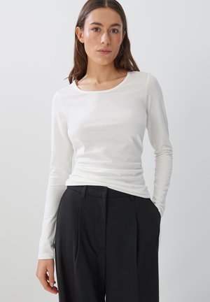 White long-sleeve shirt with a rounded neckline. Soft, smooth texture. Paired with black high-waisted trousers, featuring a tailored design.
