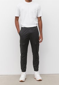 Černé cargo kalhoty s elastickými manžetami, předními kapsami a volným střihem, spárované s jednoduchým bílým tričkem a bílými teniskami.