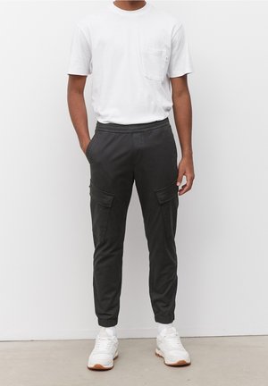 Zwarte cargobroek met elastische boorden, voorzakken en een losse pasvorm, gecombineerd met een effen wit T-shirt en witte sneakers.