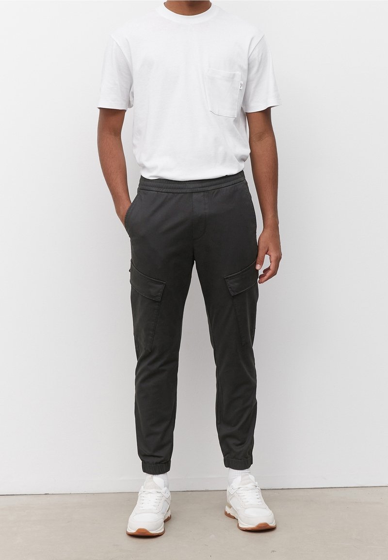 Černé cargo kalhoty s elastickými manžetami, předními kapsami a volným střihem, spárované s jednoduchým bílým tričkem a bílými teniskami.