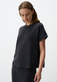 Czarna koszulka z krótkim rękawem, wykonana z gładkiego materiału, z okrągłym dekoltem i lekko luźnym krojem. Charakterystyczne elementy designu to podwinięte mankiety.