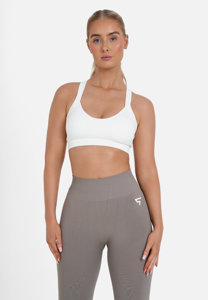 Sostén deportivo blanco con una banda ancha y tirantes ajustables, combinado con leggings de cintura alta en tono topo que presentan un pequeño logo blanco.