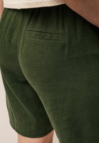 Grønne linnedshorts med et tekstureret stof, elastisk talje og en detalje med baglomme. Shortsene har en afslappet pasform og mid-tigh længde.