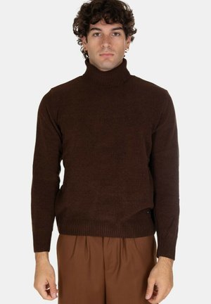Maglione a collo alto marrone realizzato in un tessuto a maglia testurizzato, con maniche lunghe e un design aderente. Indossato con pantaloni marroni.