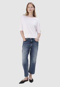 Witte cropped t-shirt met korte mouwen, gecombineerd met lichtblauwe, licht beschadigde rechte jeans. Zwarte instapschoenen. Minimalistisch ontwerp.