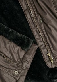 Veste en cuir synthétique marron avec doublure en fausse fourrure noire, dotée d'une fermeture éclair métallique et de détails à bouton-pression à l'avant. Texture lisse sur l'ensemble.