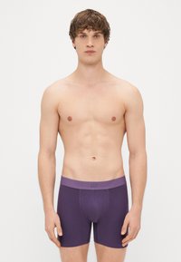 Boxers em algodão roxo com um cós em contraste. Apresenta um logo no cós e um design ajustado, textura suave e corte médio.