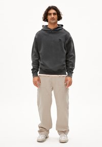 Felpa grigia scura in tessuto morbido con tasca a marsupio, indossata sopra una maglietta rosa chiaro; abbinata a pantaloni cargo beige e sneakers.