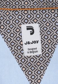 Textiellabel met een geometrisch zwart-wit patroon, benadrukt met blauwe en oranje vierkanten, bevestigd aan lichtblauwe stof.