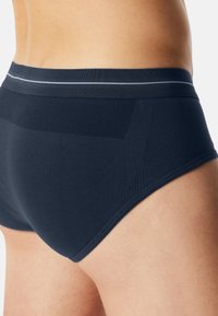 Close-up van een persoon die donkerblauwe naadloze slips draagt met een gestructureerde tailleband en een ademend mesh-paneel aan de zijkant.