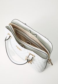 Borsa bianca trapuntata con rifiniture nere, doppie cerniere e hardware in tonalità dorata. L'interno presenta più scomparti e foderato con il logo del marchio.