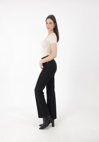 Top ajustado beige, pantalones vaqueros negros de campana y botas de tacón negras. Texturas suaves, diseño elegante y una paleta de colores neutros.
