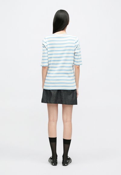 Ριγωτό μπλε και λευκό κοντομάνικο μπλουζάκι φτιαγμένο από ελαφρύ ύφασμα, συνδ�υασμένο με μια σκούρα τζιν φούστα και μαύρες κάλτσες ως το γόνατο.