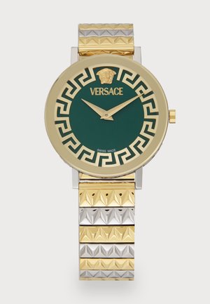 Versace ura z okroglo zlatim ohišjem, zeleno rebrastim številčnico, zlatimi urnimi kazalci in dvojnim kovinskim pasom z piramidnimi detajli.