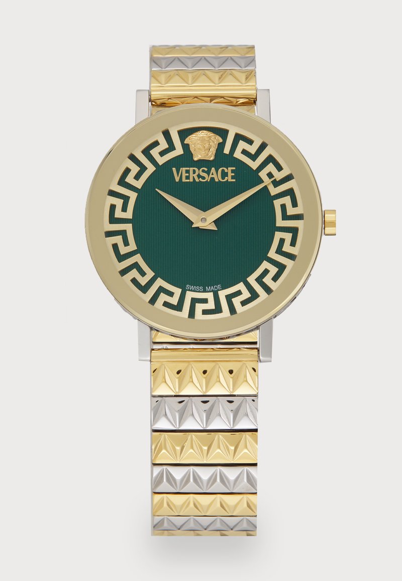 Montre Versace avec un boîtier rond en or, un cadran strié vert, des index horaires en or et un bracelet en métal bicolore avec des accents pyramides.