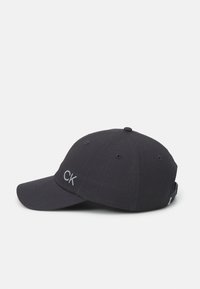 Musta puuvillainen baseball-lippalakki, jossa on kaareva lippa. Varustettu harmaalla brodeeratulla "CK"-logolla. Kuuden paneelin muotoilu tuuletusaukoilla.