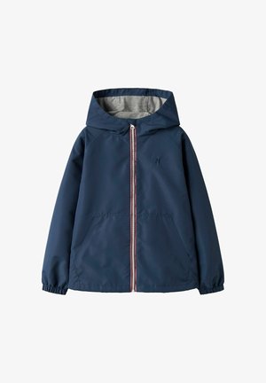 Chaqueta cortavientos de color azul marino con capucha, forro gris, puños elásticos y cremallera frontal con un acento en rojo y blanco. Dos bolsillos laterales.