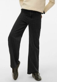 Crne traperice širokih nogavica s bijelim okomitim prugama; izrađene od trapera, s pojasom srednjeg rasta i opuštenim krojem na nogavicama.