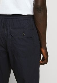 Shorts bleu marine à coupe décontractée, dotés d'une poche arrière avec fermeture à bouton et d'un tissu texturé. Design simple de la ceinture.