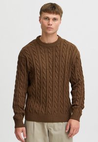 Brown cable-knit sweater with texture, crew neckline, and ribbed cuffs. Features a relaxed fit and distinctive raised patterns throughout.
