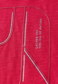 Červená textilie s hladkým povrchem, s kontrastními světle modrými akcenty v geometrickém designu a vyšívanou frází: "SHROMAŽĎUJTE POCIT PŘÍRODY."