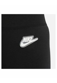 Czarne legginsy sportowe z srebrnym logo Nike w formie podklejki z charakterystycznym swooshem po lewej stronie. Gładki, elastyczny materiał.