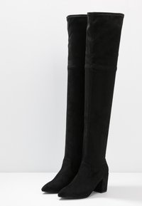 Sorte over-the-knee-støvler lavet af ruskind, med spids tå og en kraftig blokhæl, med en glat tekstur og uden synligt metaludstyr.