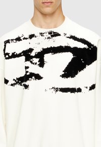 Sudadera blanca hecha de una tela suave, con un gran estampado abstracto negro en la parte frontal, cuello redondo y mangas largas.