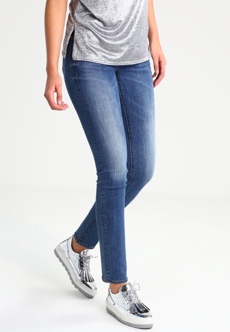 Jeans ajustados azules con un acabado desgastado, combinados con una blusa plateada brillante y zapatillas metálicas con detalles de flecos.