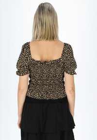 Leopardenmuster Bluse mit kurzen Puffärmeln, gerafftem Smocking auf der Rückseite und schwarzem elastischen Bund. Schwarzer schichtierter Rock an der Unterseite.