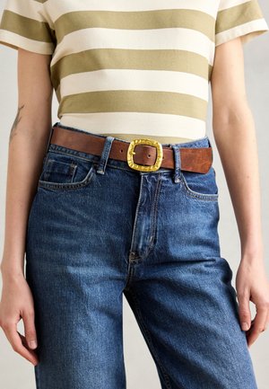 Bruine leren riem met een gestructureerde gouden metalen gesp, gedragen met een gestreepte kaki en crèmekleurige t-shirt en blauwe spijkerbroek.