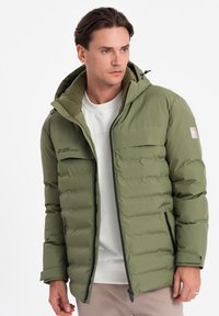 Olivově zelená zateplená bunda s horizontálním prošíváním, černým zipem, nastavitelnou kapucí a dvěma bočními kapsami. Hladká textilie.